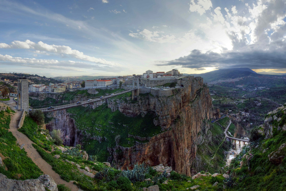 View of a buildings and a bridge sitting over cliffs with sunset in the background