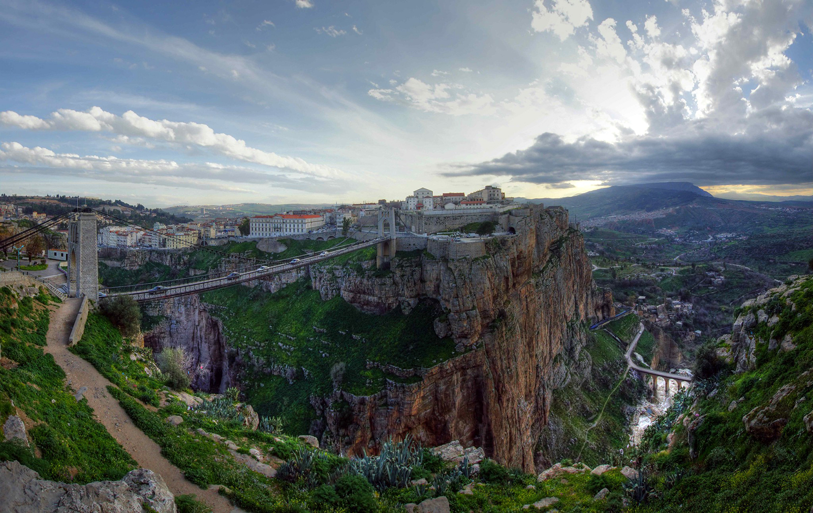 View of a buildings and a bridge sitting over cliffs with sunset in the background