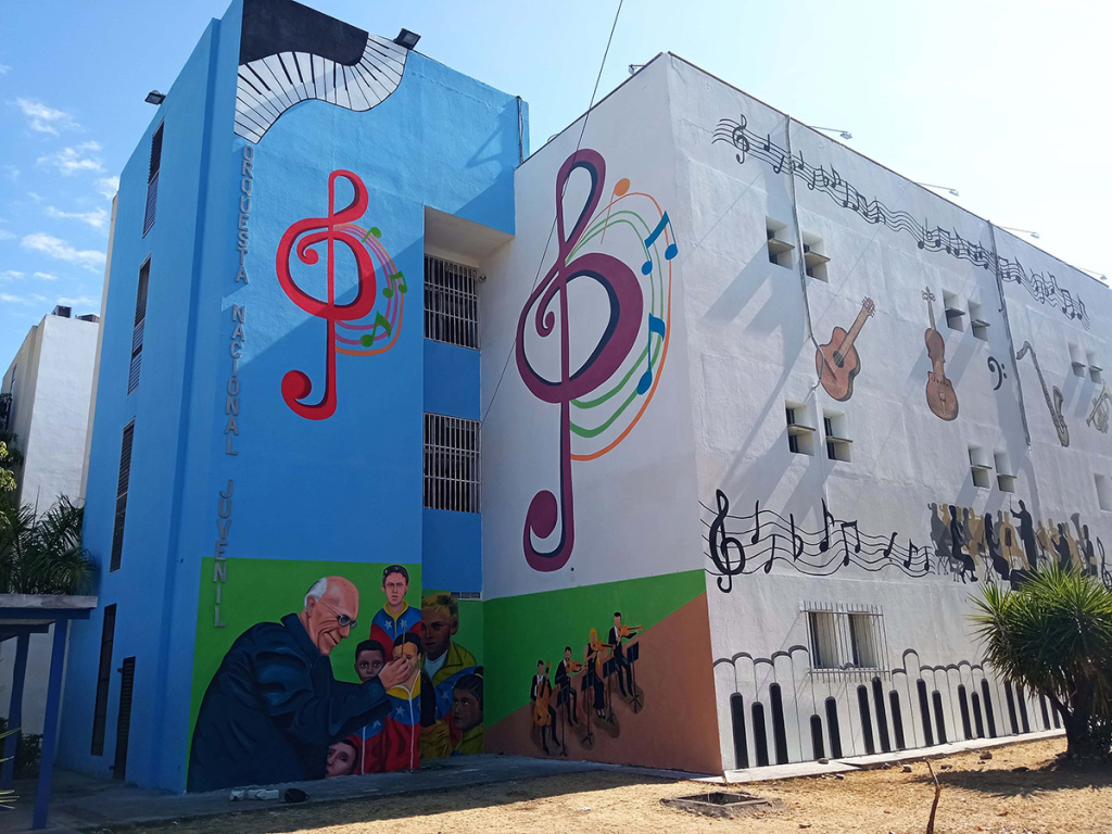 Building exterior in blue and white, with musical notes, piano keys, and other instruments painted on the walls. A mural on the bottom left shows an elderly man conducting a children's choir and musicians.